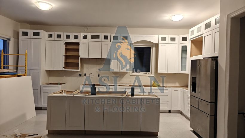 White shaker kitchen cabinets mid-installation with glass-front upper cabinets