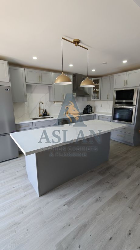 Grey shaker kitchen with a white quartz island, brass pendants and built-in wall ovens