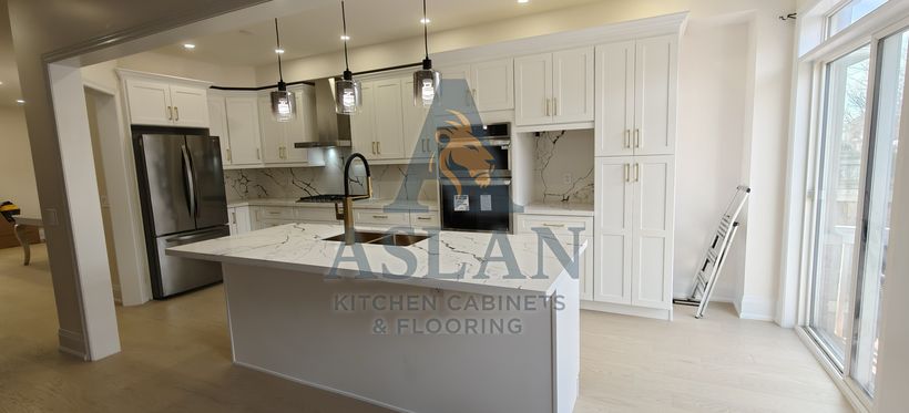 Open white shaker kitchen with wall ovens, glass pendants and marble-look quartz island