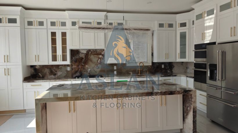 Close view of a natural stone waterfall island and full-height stone backsplash with white shaker cabinets and gold hardware